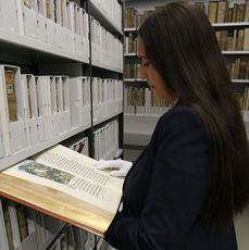 Mitarbeiterin hat ein altes Buch aufgeschlagen und liest darin.