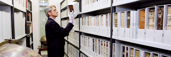 Ein Mitarbeiter nimmt ein in Karton gehülltes altes Buch aus dem Regal in der Schatzkammer