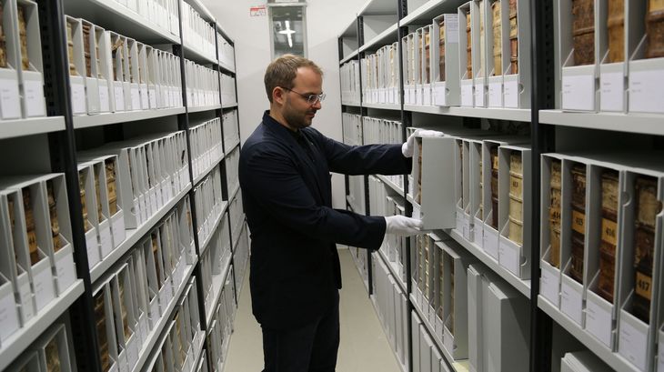 Mitarbeiter steht vor einem Regal mit alten Büchern und nimmt ein Buch aus dem Regal.